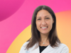 A smiling image of Laura Soucek in a lab coat against a branded Worldwide Cancer Research backdrop in yellow and pink